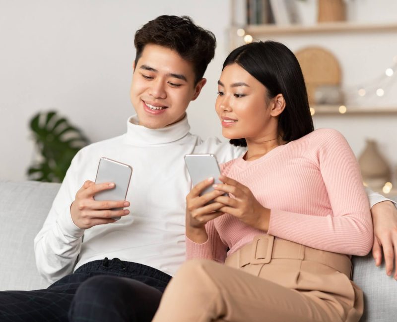 asian-couple-using-smartphone-phones-browsing-internet-sitting-at-home-1.jpg